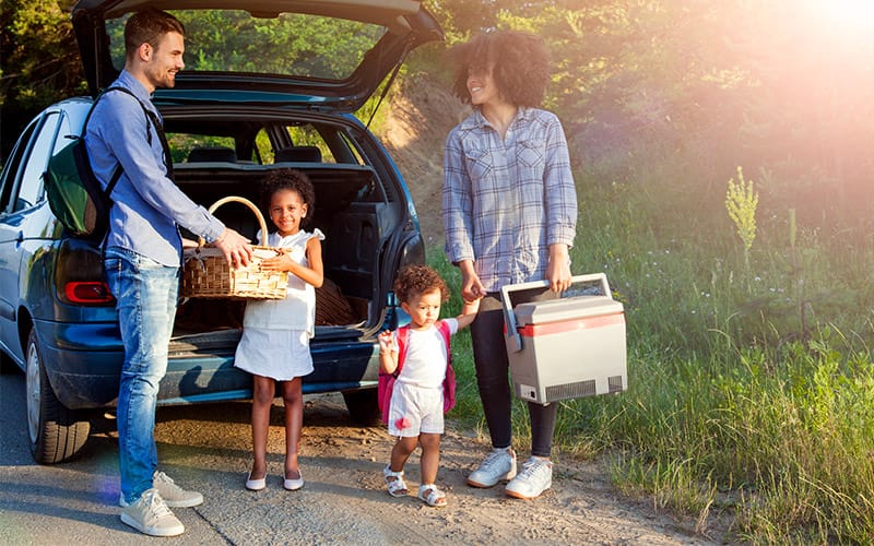 Familia de raza mixta sacando cosas del coche de alquiler para picnic